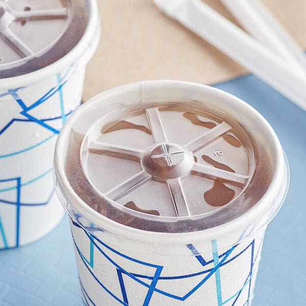 Choice translucent plastic lids on two cups with straws on a table.