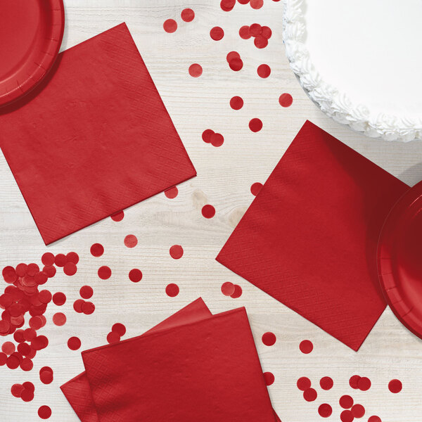 A table with red napkins and confetti.