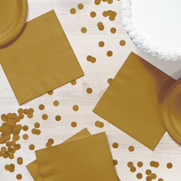 A table with a white Creative Converting Glittering Gold luncheon napkin and confetti.