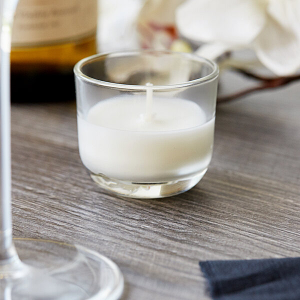 A Sterno PetiteLites clear wax candle in a glass on a table