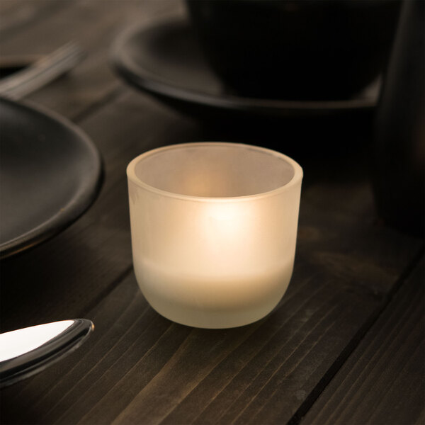 A Sterno PetiteLites wax candle in a glass holder on a table.