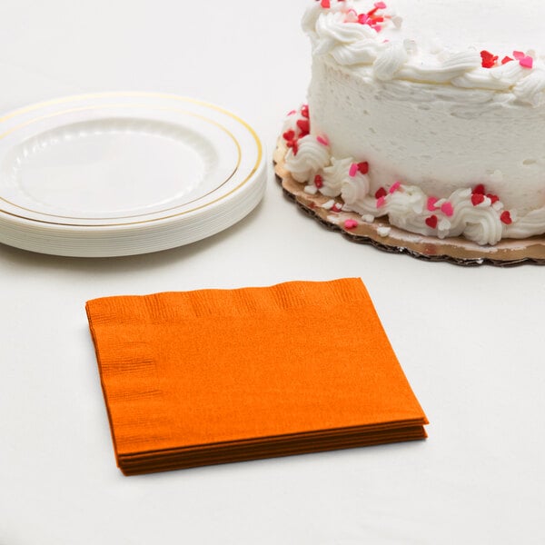 A white cake with red and pink sprinkles next to a stack of orange napkins.