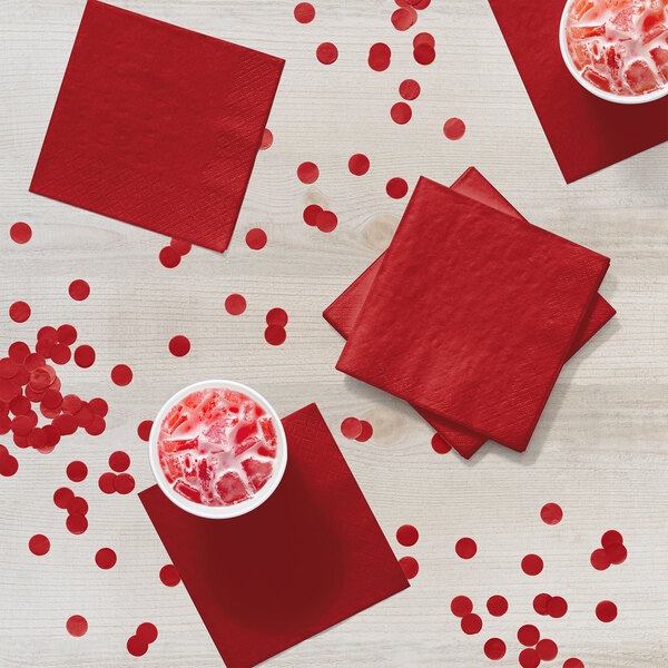A group of cups of red drinks with Classic Red Creative Converting beverage napkins.
