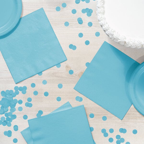 A table with blue napkins and confetti next to a blue plate.