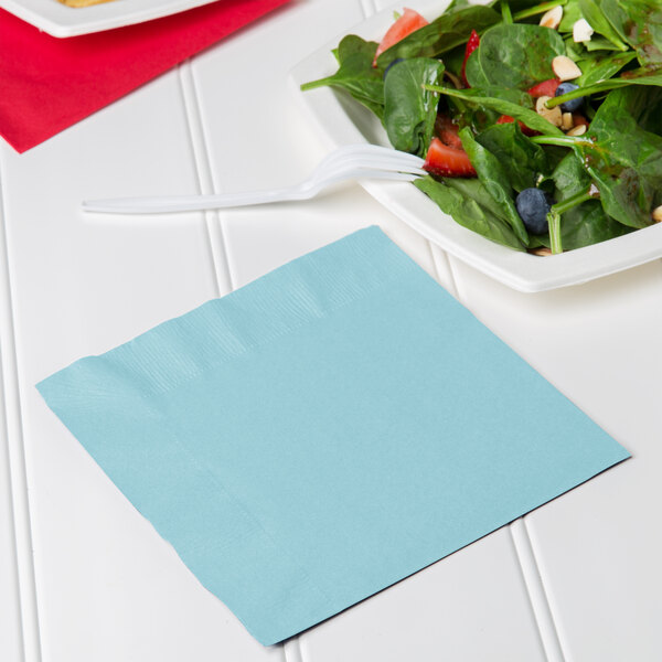 A pastel blue luncheon napkin with a fork and salad on a plate.