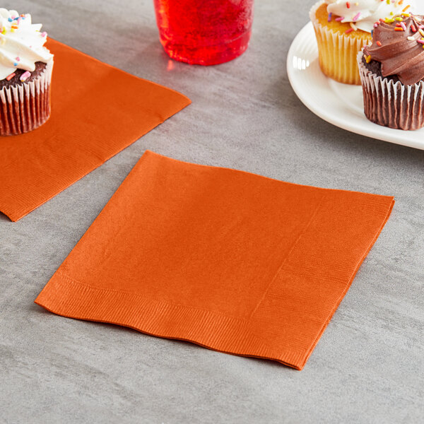 A plate of Creative Converting Sunkissed Orange 3-ply luncheon napkins with cupcakes on a table.