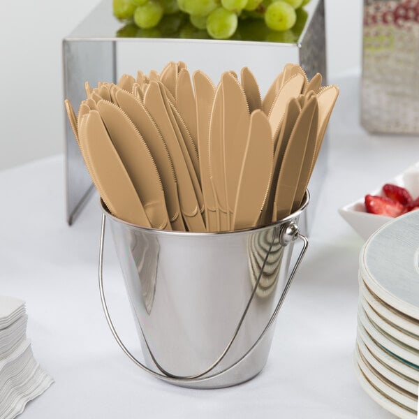 A bucket of Creative Converting Glittering Gold plastic knives on a white surface.