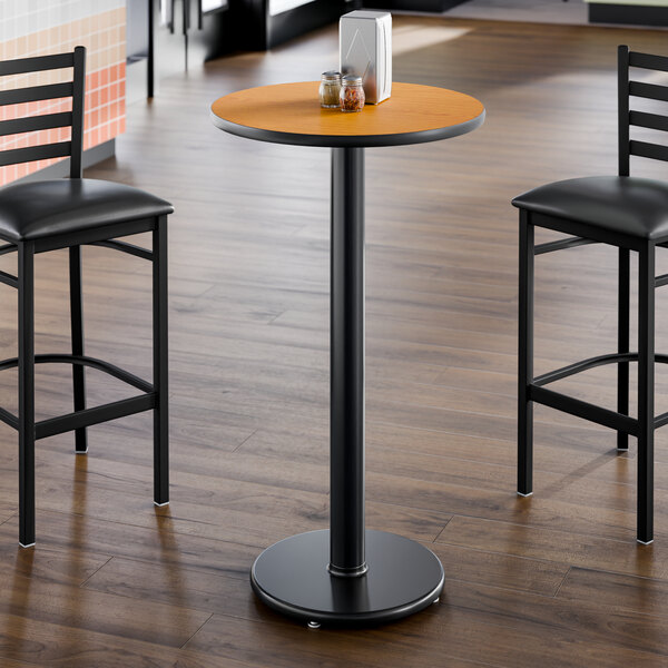 A round, 24-inch laminated table with a reversible walnut and oak finish, shown with a black pedestal base in a dining setting.
