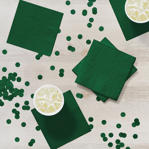 A Hunter Green Creative Converting beverage napkin on a table with a cup of iced tea.