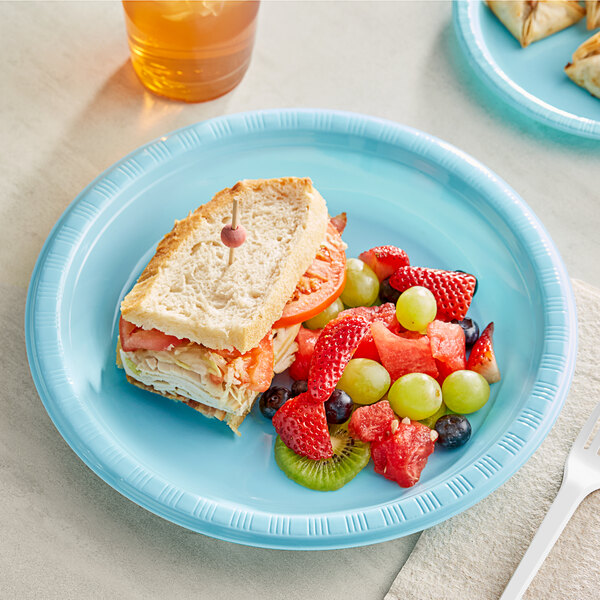 A Creative Converting pastel blue plastic plate with a sandwich, fruit, and a glass of juice.