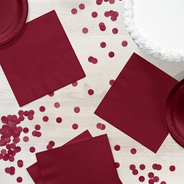 A table with burgundy napkins and confetti.