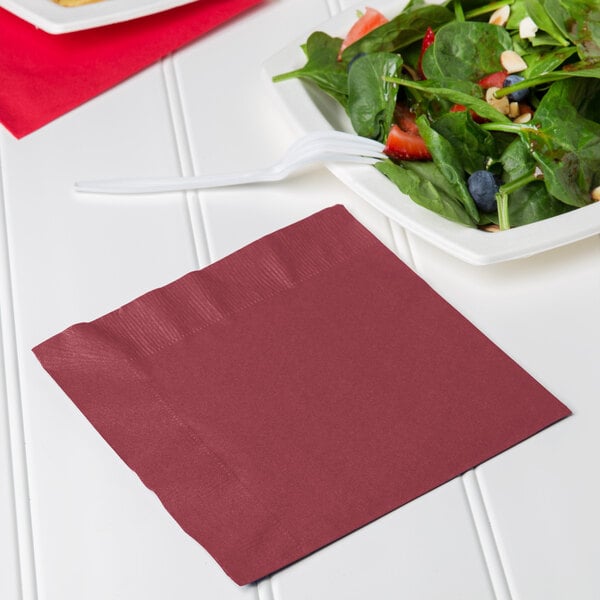 A plate with a bowl of salad and a burgundy luncheon napkin with a fork on top.