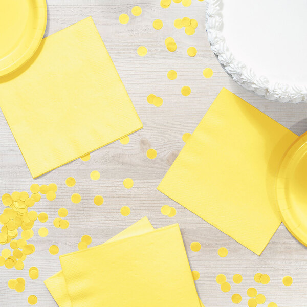 A table with yellow napkins and a cake with yellow polka dots on a white surface.