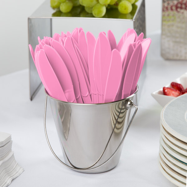 A bucket filled with pink plastic knives.