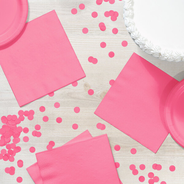 A pink Creative Converting luncheon napkin and confetti on a white table.