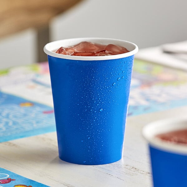 A close-up of a blue Creative Converting paper hot/cold cup with ice and a brown drink inside.