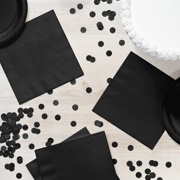 A table with black napkins and confetti.