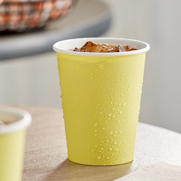 A Creative Converting mimosa yellow paper cup with ice water in it.