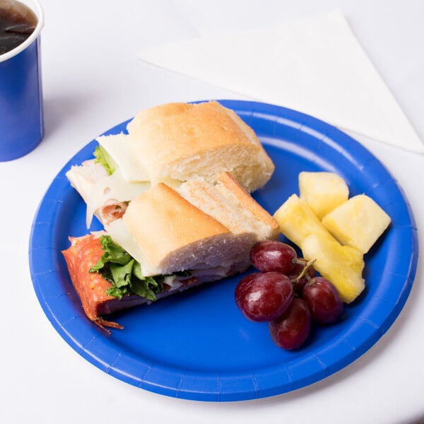 A sandwich with meat and cheese on a cobalt blue Creative Converting paper plate.