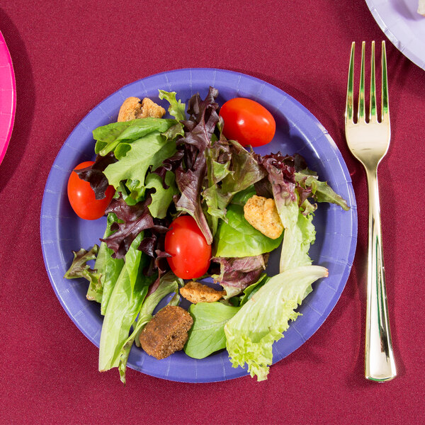 A purple Creative Converting paper plate with a fork and knife on a table with a salad