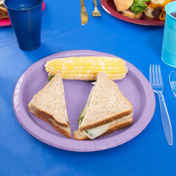 A Creative Converting Luscious Lavender paper plate with a sandwich and corn on it.