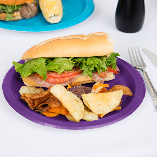 A sandwich and chips on a Creative Converting amethyst purple paper plate with a fork and knife.