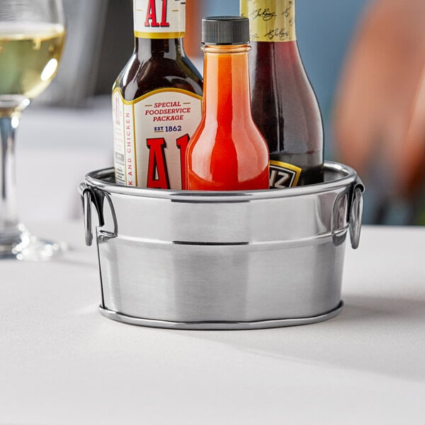 An American Metalcraft stainless steel round metal tub holding bottles of sauce on a table.