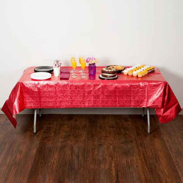 A table with a red Creative Converting table cover and food on it.