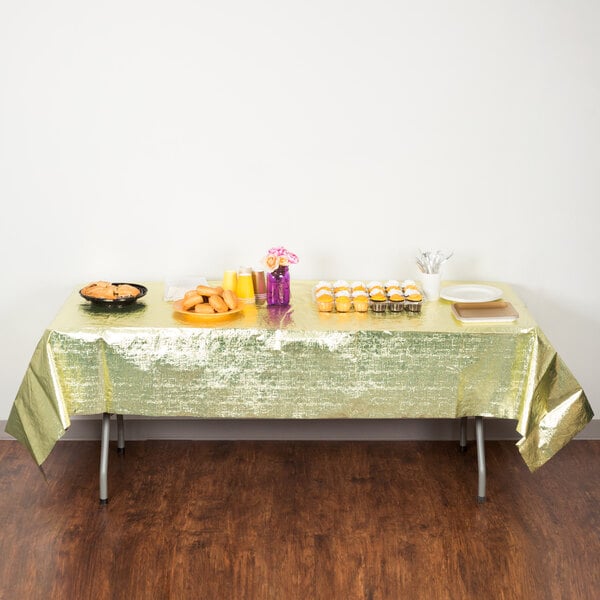 A table with a Creative Converting gold metallic plastic table cover with food on it.