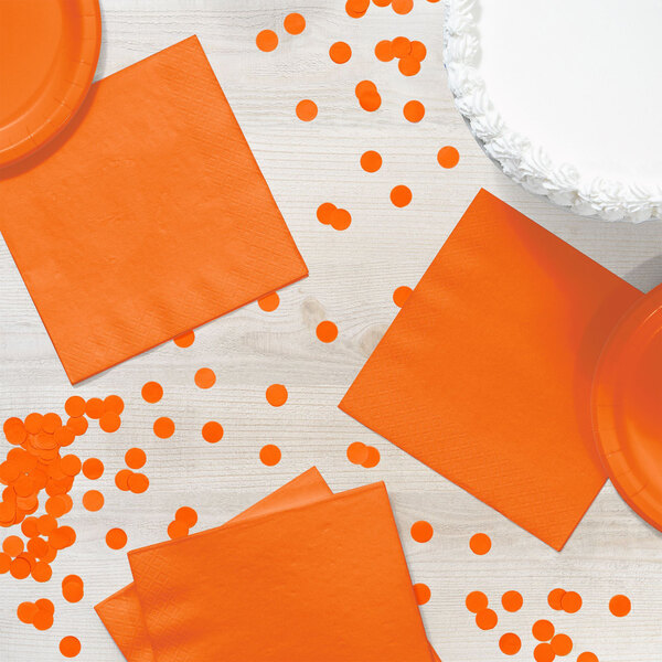 An orange paper napkin with a white dot pattern on a table with confetti.