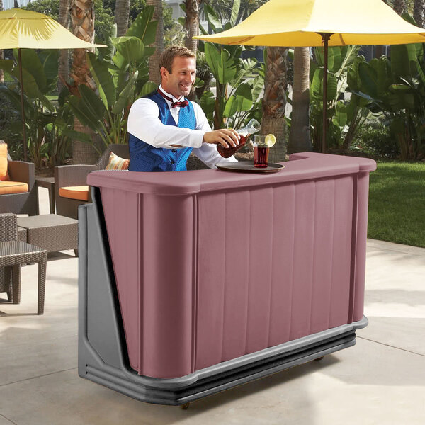 A man standing behind a Cambro mahogany portable bar with a drink.