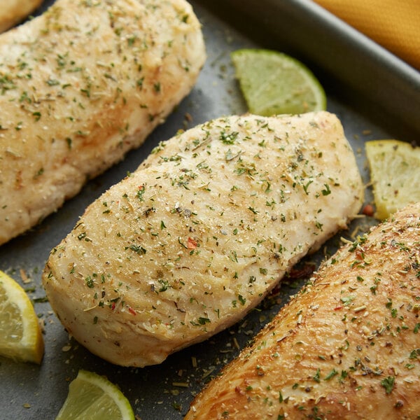 A tray of chicken breasts seasoned with Regal Herbs & Garlic Blend and garnished with lemon slices and herbs.