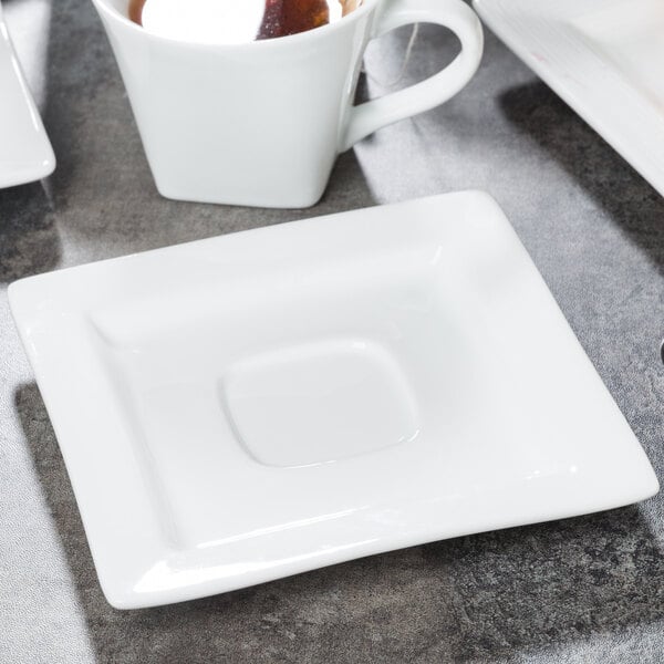 A Libbey white square porcelain saucer with a well ring on a table with a cup of tea.