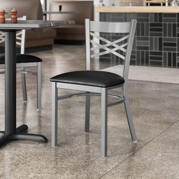 A Lancaster Table & Seating silver metal chair with a black cushion at a table in a restaurant.