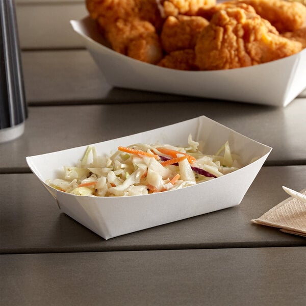 A white paper food tray with coleslaw and chicken wings on a counter.