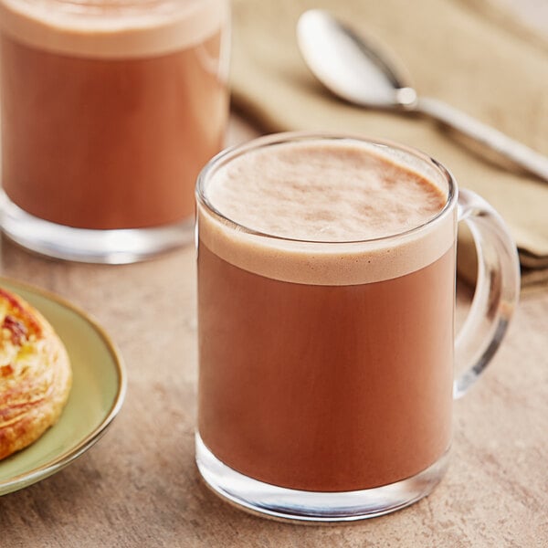 A glass mug of Ghirardelli sweet ground chocolate on a plate with a pastry.