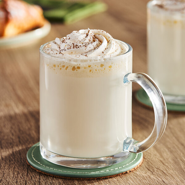 A glass mug of white Ghirardelli Sweet Ground White Chocolate coffee with whipped cream.