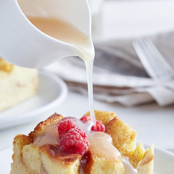 A white pitcher of Ghirardelli White Chocolate Sauce being poured onto a dessert.