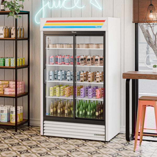 A white refrigerated sliding glass door merchandiser with LED lighting, stocked with various beverages.