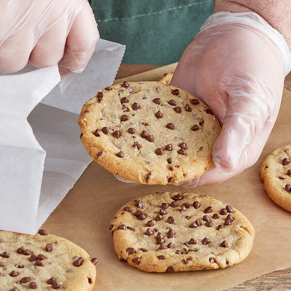 A person in plastic gloves holding a chocolate chip cookie with Ghirardelli Barista Dark Chocolate Chips.