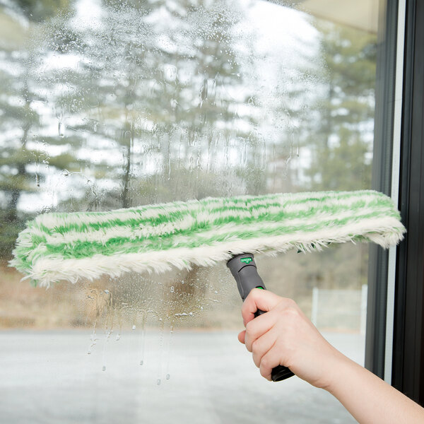 A hand using a Unger Monsoon Plus StripWasher Sleeve to clean a window.