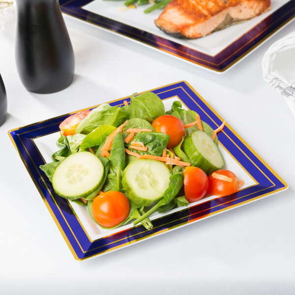 A Fineline white plastic plate with blue rim and gold bands holding salad with tomatoes and cucumbers.