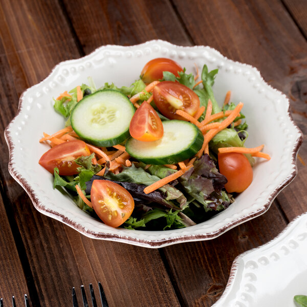 A 10 Strawberry Street Oxford cream stoneware salad bowl filled with a salad with cucumbers, tomatoes, and lettuce with a fork.