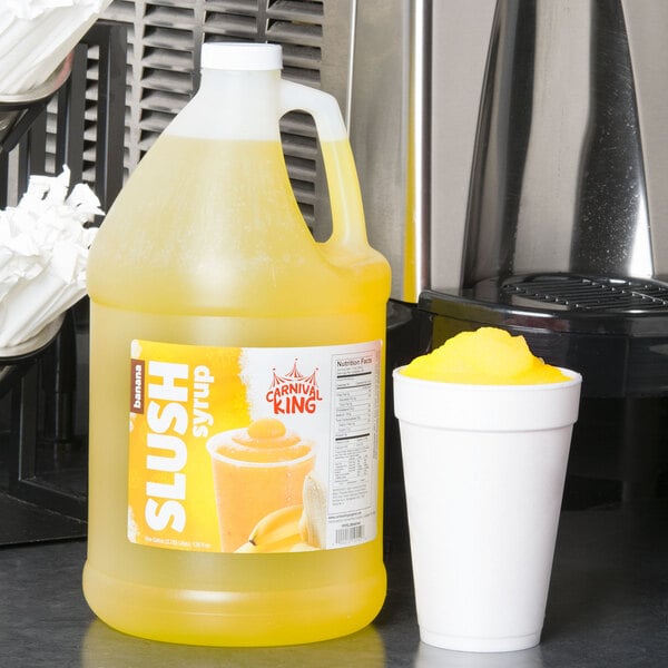 A jug of Carnival King Banana Slushy Concentrate next to a cup of slushy drink.