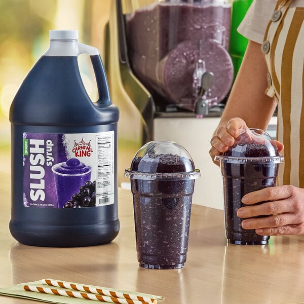 A gallon jug of Carnival King grape slush syrup concentrate next to two cups of prepared grape slushies.