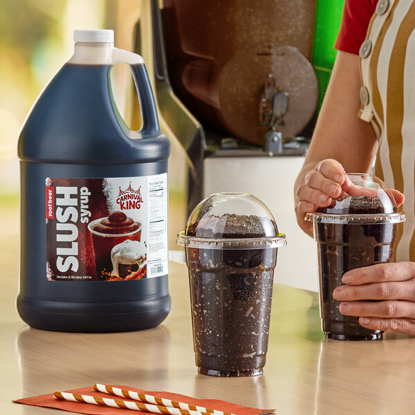 A gallon jug of Carnival King root beer slush syrup concentrate next to two cups of prepared root beer slushies.