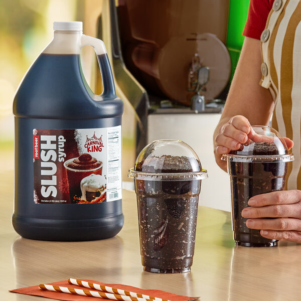 A gallon jug of Carnival King root beer slush syrup concentrate next to two cups of prepared root beer slushies.