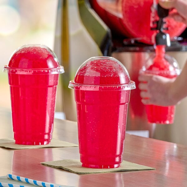 A clear plastic cup filled with bright red cherry slushy and topped with a domed lid.