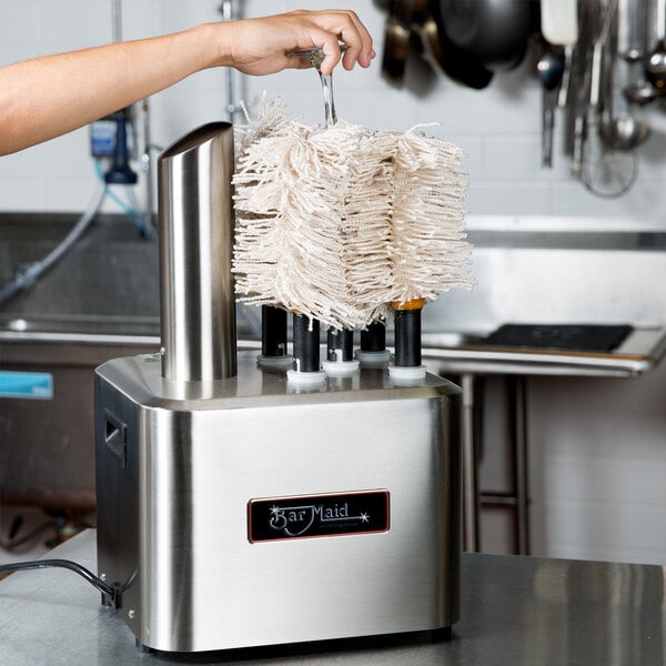 A woman using a Bar Maid electric glass polisher brush on a counter in a professional kitchen.