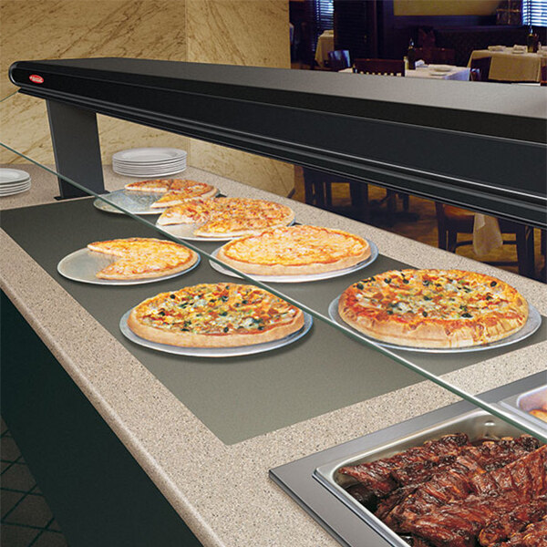 A Hatco built in heated shelf with pizzas on plates in a hotel buffet.